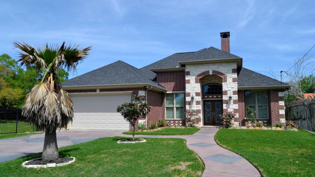 A modern, single-family house with a green lawn and a paved driveway, set against a clear blue sky.